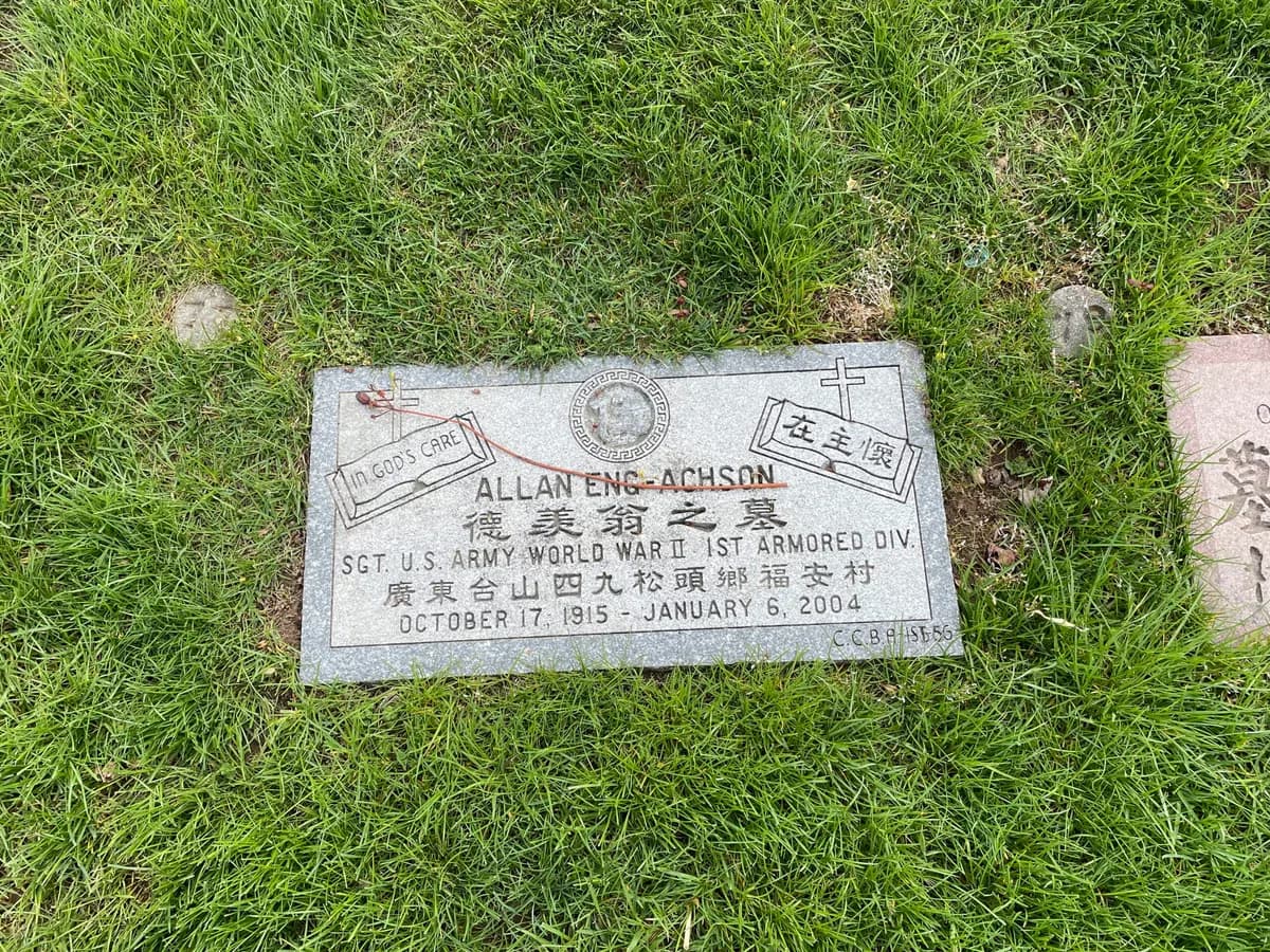 Flat grey granite footstone set flush in grass, carrying a United States Army service emblem beside lettering in Chinese and English.